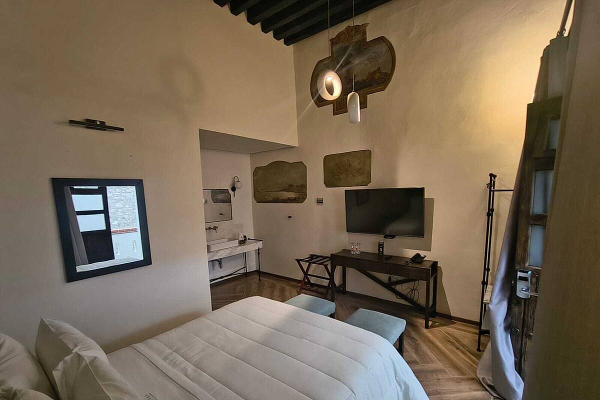 Ein Schlafzimmer mit einem Bett, einem Schreibtisch mit Fernseher, einem Spiegel und Kunstwerken an den Wänden.