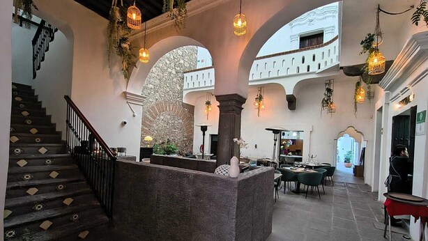 Un'ampia hall con una scala in pietra, soffitti a volta, lampadari e un'area salotto centrale.