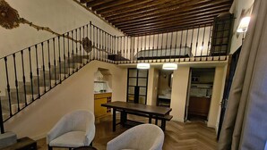 Un'ampia zona giorno con una scala, un tavolo da pranzo, due poltrone e una cucina sullo sfondo.