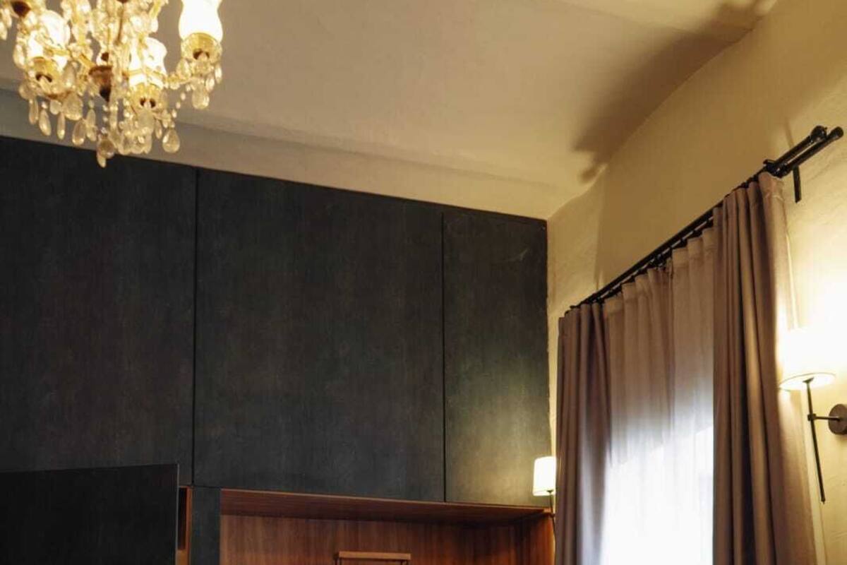 Ein modernes Zimmer mit einem dunklen Holzschrank, einer Kristallleuchter, einem Esstisch mit Stühlen und einem großen Fenster mit Vorhängen.