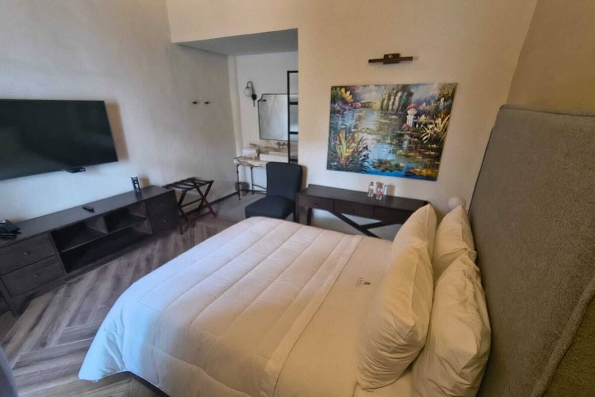 Ein Hotelzimmer mit einem Bett, einem Schreibtisch, einem Sessel, einem Fernseher und einem Bild an der Wand.
