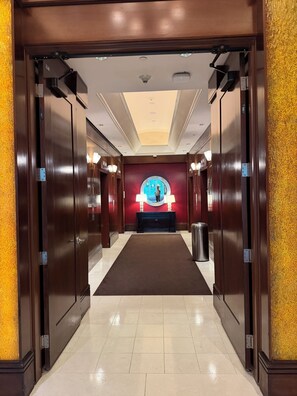 A hotel corridor with wooden doors, a marble floor, a reception desk with a blue and white color scheme, and a ceiling with recessed lighting. - AWESOME ONE BEDROOM HIGH RISE PENTHOUSE WITH BALCONY, AMAZING STRIP VIEW !! (Las Vegas)