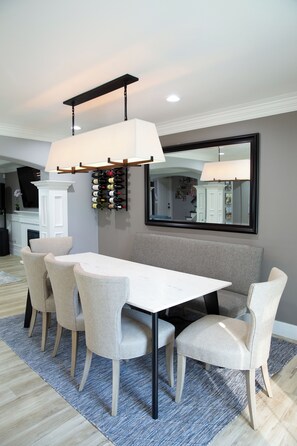 A dining area with a white table, four chairs, a blue rug, and a wine rack on the wall. - Modern, Luxury & Cozy 3 Beds/ 2 Baths Home in Evergreen (San Jose)