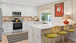 A modern kitchen with white cabinets, stainless steel appliances, a marble island, and a red poster on the wall. - Stylish Two Bedroom House in Peaceful Neighborhood (Carlsbad)