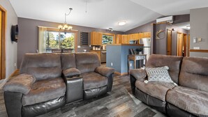 A modern living room with leather sofas, a chandelier, and a view of the kitchen and dining area.