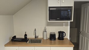 Kompakti keittiö, jossa on valkoiset kaapit, mikroaaltouuni, pesuallas ja työtaso, jonka päällä on leivänpaahdin ja vedenkeitin.