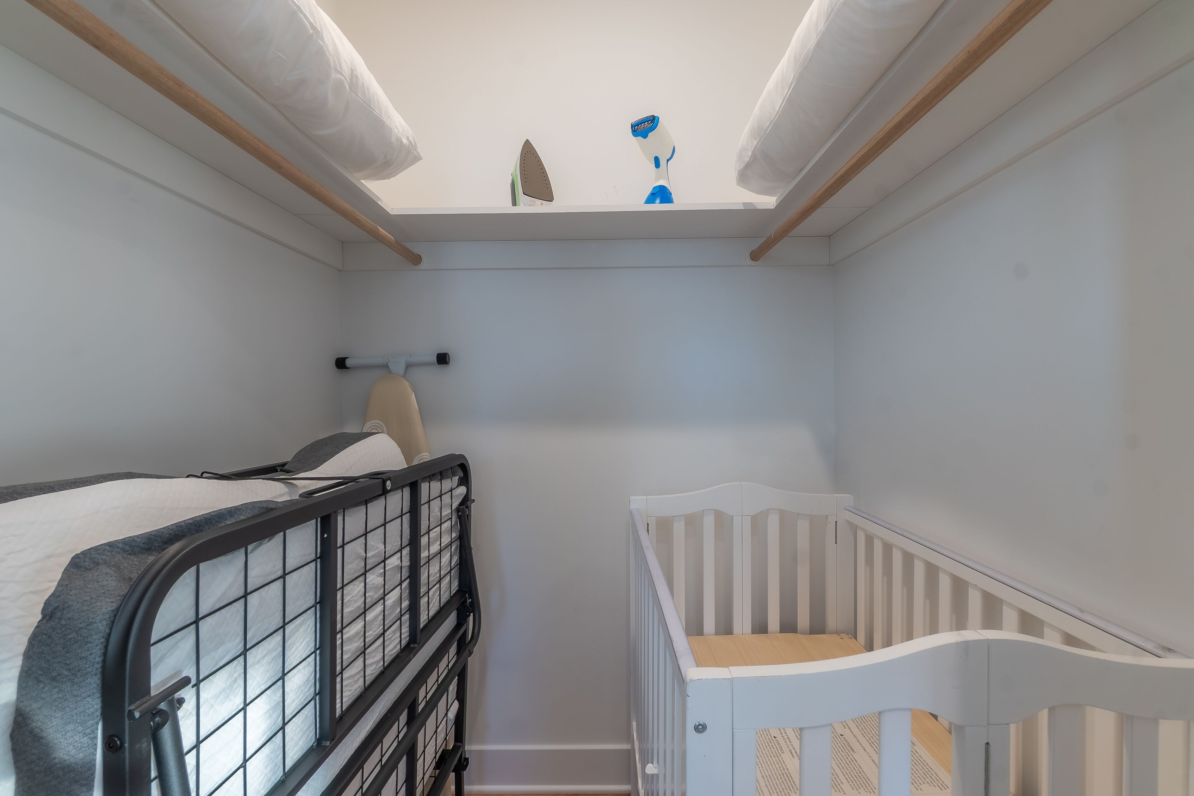 A small, well-lit room with a bunk bed and a crib, featuring a skylight and a wooden ceiling beam.