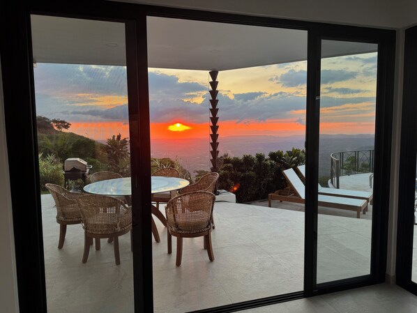 Une pièce dotée d’une porte vitrée donnant sur un balcon d’où l’on peut admirer un coucher de soleil sur la ville.