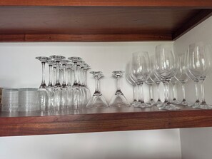 Une étagère en bois sur laquelle sont disposés de manière ordonnée divers objets en verre transparent, notamment des verres à vin et des verres à cocktail.