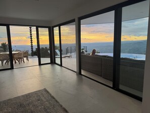 Une pièce spacieuse dotée de grandes portes-fenêtres coulissantes donnant sur un balcon avec vue sur l’océan et le coucher de soleil.