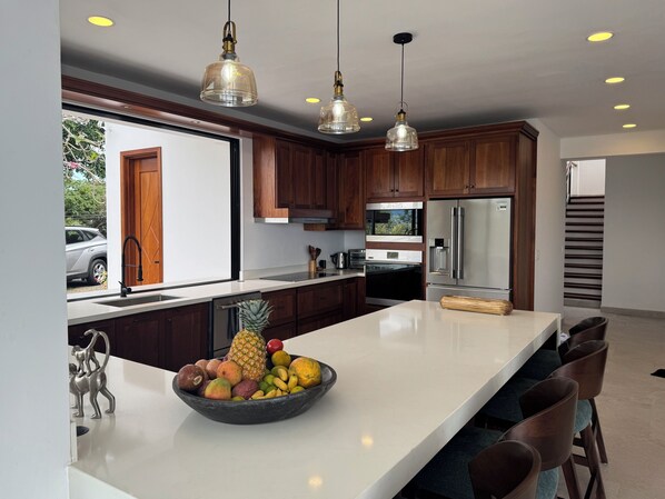 A modern kitchen with wooden cabinets, stainless steel appliances, and a large island with a fruit bowl.