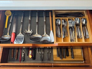 Un tiroir contenant divers ustensiles de cuisine, notamment des cuillères, des spatules et des couteaux, rangés dans des compartiments.