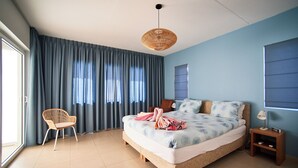 A bedroom with a large bed, a chair, a bedside table, and a window with curtains. - 2-bedroom apartment in Blue Bay Resort (Willemstad)