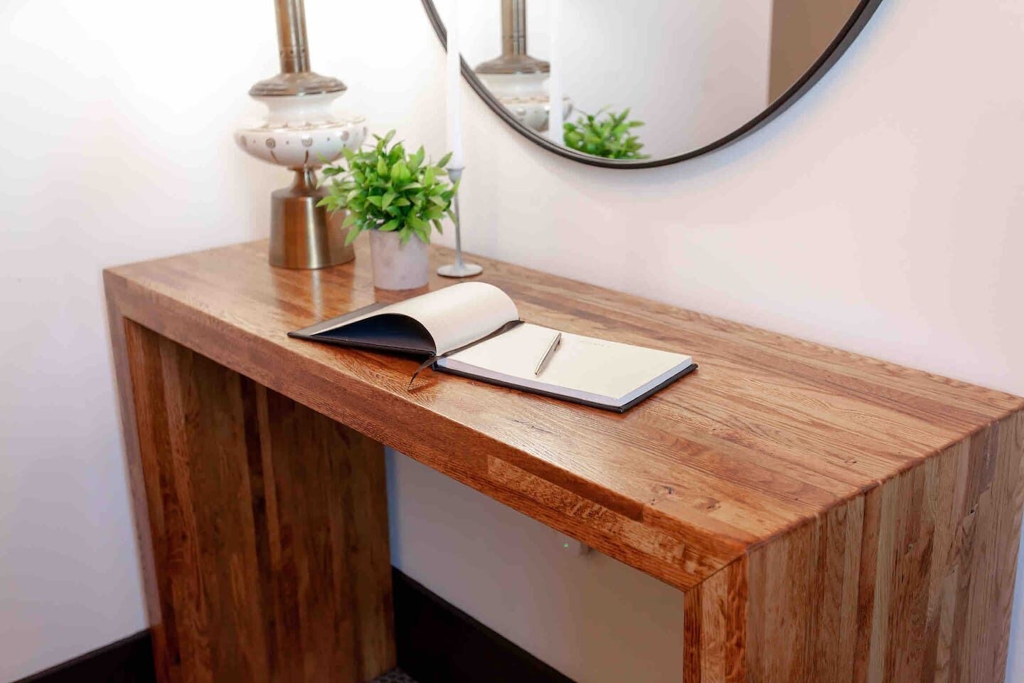 A wooden console table with a notebook and pen, a small potted plant, and a lamp.