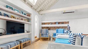 Een woonkamer met een televisie, zitmeubels en planken met ingekaderde foto's.