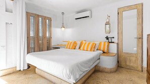 Een slaapkamer met een groot bed, een houten bankje, een nachtkastje, een airconditioning en een deur met houten frame.