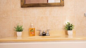 A bathroom with a mirror, two sinks, a soap dispenser, and two potted plants. - The Hideaway (St. Ann Parish)