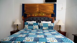 A bed with a blue and white quilt, two bedside lamps, and a wooden headboard with curtains. - The Hideaway (St. Ann Parish)