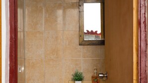 A bathroom with beige tiles, a wooden door, a small sink with a mirror, and a plant on the counter. - The Hideaway (St. Ann Parish)