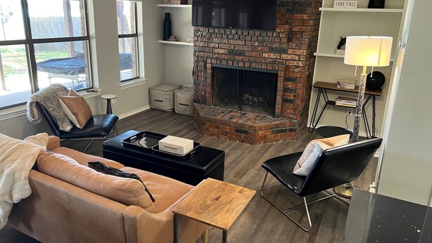 A living room with a brick fireplace, leather sofa, and a flat-screen TV mounted above it. - Waterfront Home Minutes from Downtown Fort Worth and Stockyards (Fort Worth)