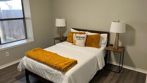 A bedroom with a bed, two bedside lamps, a window, and a wooden floor. - Waterfront Home Minutes from Downtown Fort Worth and Stockyards (Fort Worth)