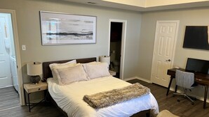 A bedroom with a large bed, bedside tables, a desk with a chair, a TV, and a door leading to a bathroom. - Waterfront Home Minutes from Downtown Fort Worth and Stockyards (Fort Worth)