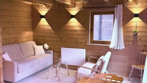 A cozy cabin interior with a sofa, chairs, a small table, and a window with curtains. - Eden Criou - Chalet sleeps 7 to 9 - pool/sauna (Morillon)