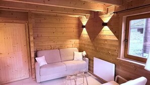 A cozy room with wooden walls, a white sofa, a small table, and a window with a view. - Eden Criou - Chalet sleeps 7 to 9 - pool/sauna (Morillon)