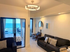 Un salon moderne avec un canapé, un fauteuil, une table et une vue sur la mer, visible à travers une porte vitrée.