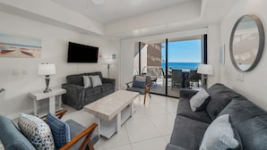 Ein modernes Wohnzimmer mit einem Flachbildfernseher, grauen Sofas, einem Couchtisch und einem Balkon mit Meerblick.