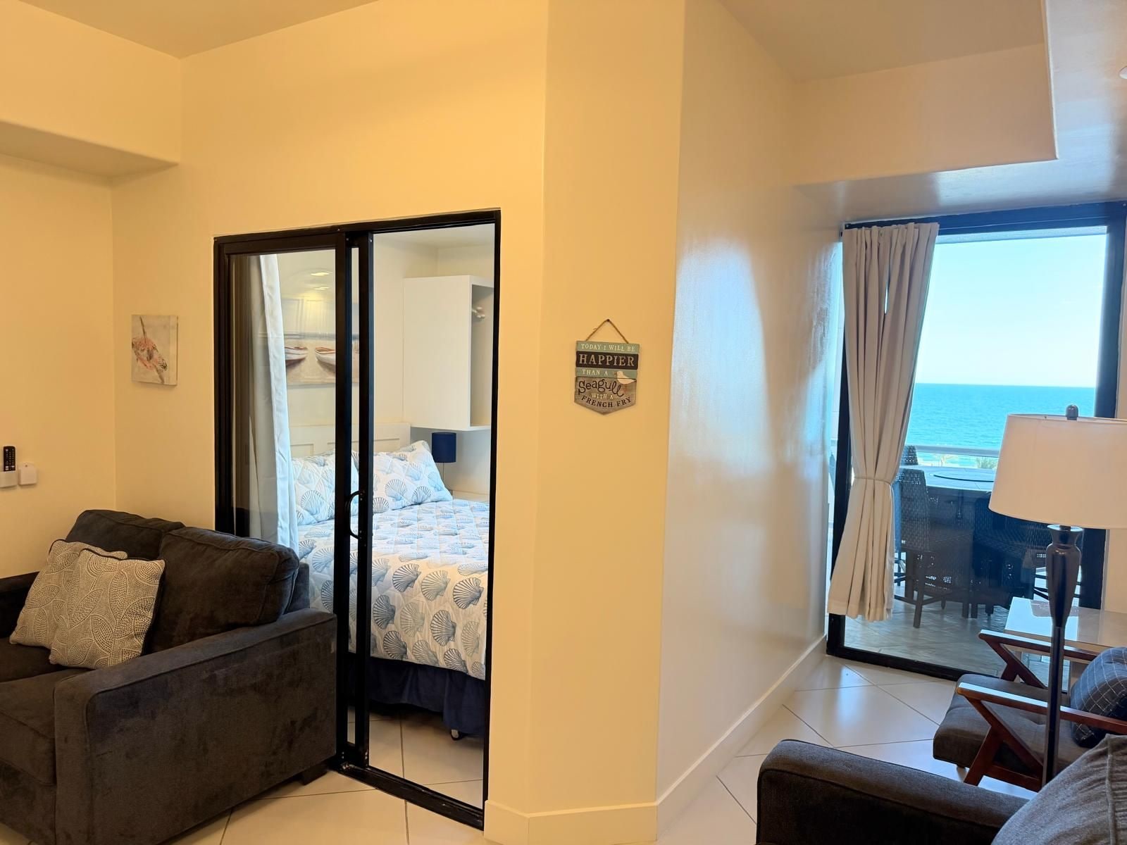 Habitación de hotel con balcón con vistas al mar, un sofá, una cama con edredón estampado y un letrero en la pared.