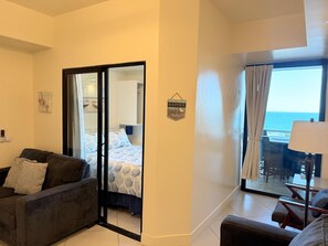 Une chambre d’hôtel avec un balcon donnant sur la mer, un canapé, un lit avec une couette à motifs et un panneau fixé au mur.