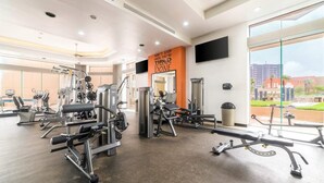 Een moderne sportschool met diverse fitnessapparaten, een groot raam met uitzicht op de stad, en een motiverende poster aan de muur.