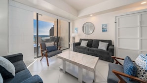Ein modernes Wohnzimmer mit einem grauen Sofa, einem Couchtisch und Blick auf die Stadt durch große Glaswände.