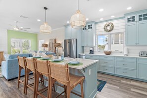 A modern kitchen with light blue cabinets, a central island with bar stools, a stainless steel refrigerator, and a ceiling fan. - 391 BLUE MOUNTAIN RD ...4 Bedrooms w/ Private Pool... STEPS TO THE BEACH! (Santa Rosa Beach)