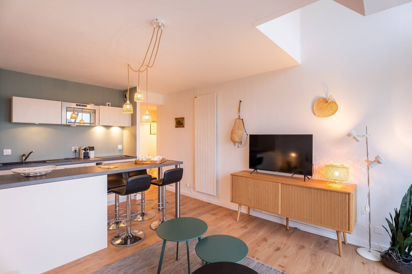 Een moderne keuken met een centraal eiland, barkrukken, een flatscreen televisie en een eettafel.