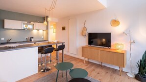 A modern kitchen with a central island, bar stools, a flat-screen TV, and a dining table. - Carnac - 3-room apartment - 50m² - Wifi - Pool (CARNAC)