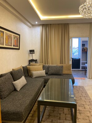 Ein modernes Wohnzimmer mit einem Ecksofa, einem Glastisch und einer Chandelier.