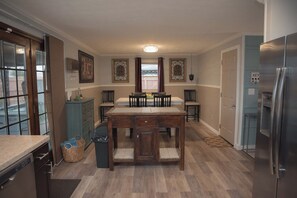 A kitchen with a wooden table, chairs, a refrigerator, and a window with curtains. - Fire Pit, Private Hot Tub + Workspace - Sleeps 7 (Dayton)