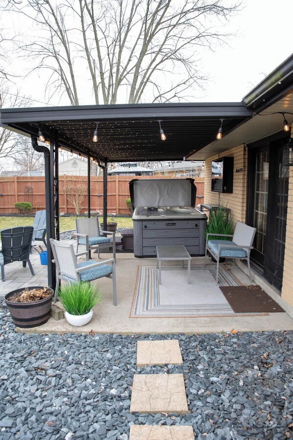 An outdoor patio with a grill, seating, and a covered area with string lights. - Fire Pit, Private Hot Tub + Workspace - Sleeps 7 (Dayton)
