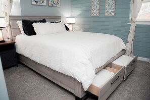 A neatly made bed with a white comforter and pillows, a bedside table with a lamp, and a wall with decorative panels. - Fire Pit, Private Hot Tub + Workspace - Sleeps 7 (Dayton)