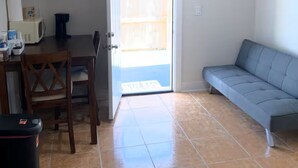 Ein Wohnzimmer mit einer Couch, einem Esstisch mit Stühlen, einem an der Wand montierten Fernseher und einer Glastür zu einem Außenbereich.