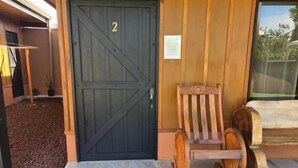 A wooden exterior with a black door marked with the number 2, a bench, and a stone-tiled entrance area. - Rusticas Dani & Fam (La Fortuna)