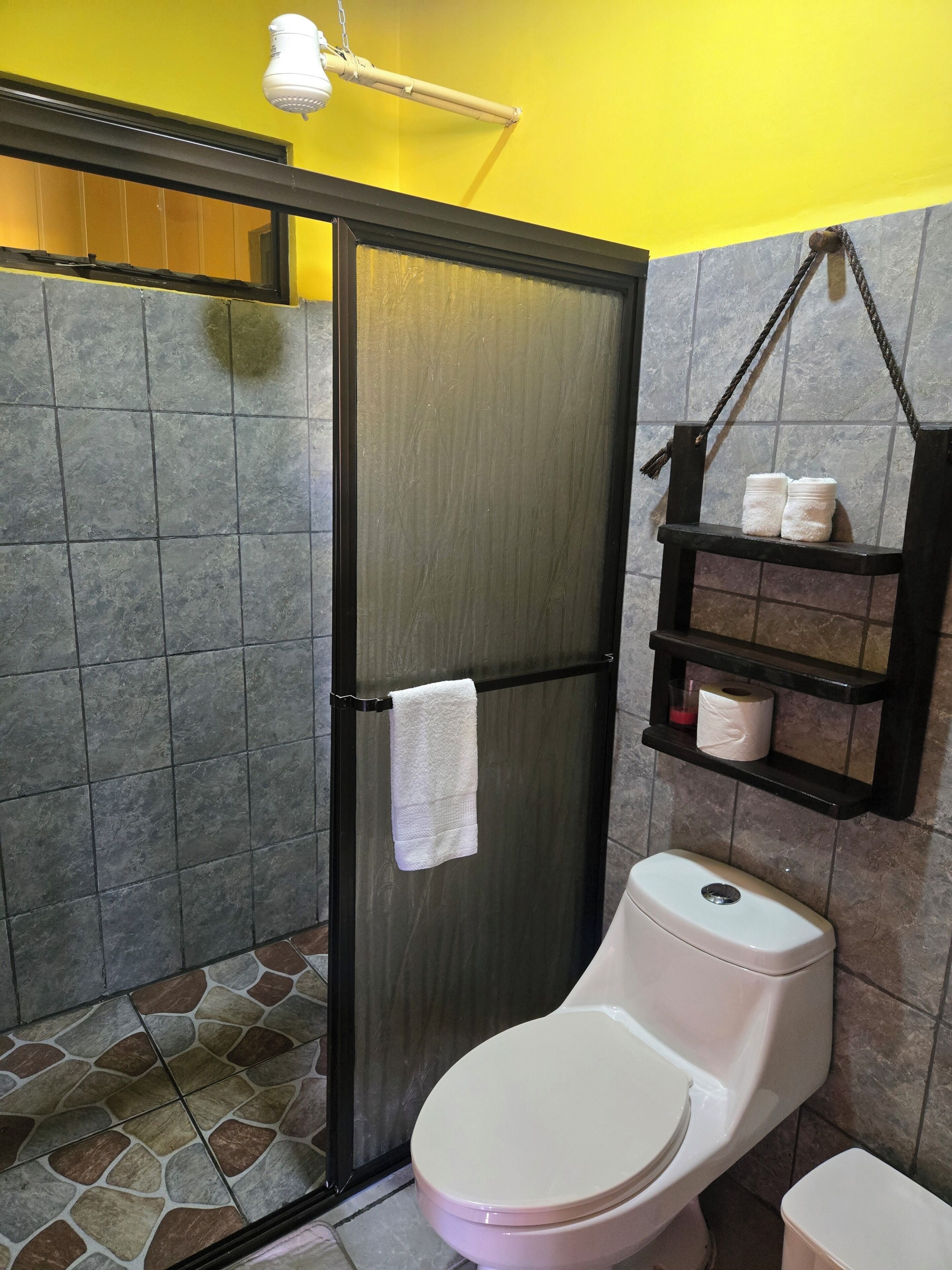 Une salle de bain avec des toilettes, une serviette accrochée à la porte et une étagère contenant des articles de toilette.
