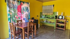 A dining area with a wooden table and chairs, a kitchen with a green countertop, and a yellow wall. - Rusticas Dani & Fam (La Fortuna)