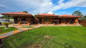 A row of two-story cabins with red-tiled roofs, a grassy lawn, and a paved walkway leading to the entrance. - Rusticas Dani & Fam (La Fortuna)