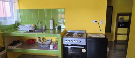 Cocina compacta con fregadero, estufa y refrigerador, con azulejos verdes y paredes amarillas.