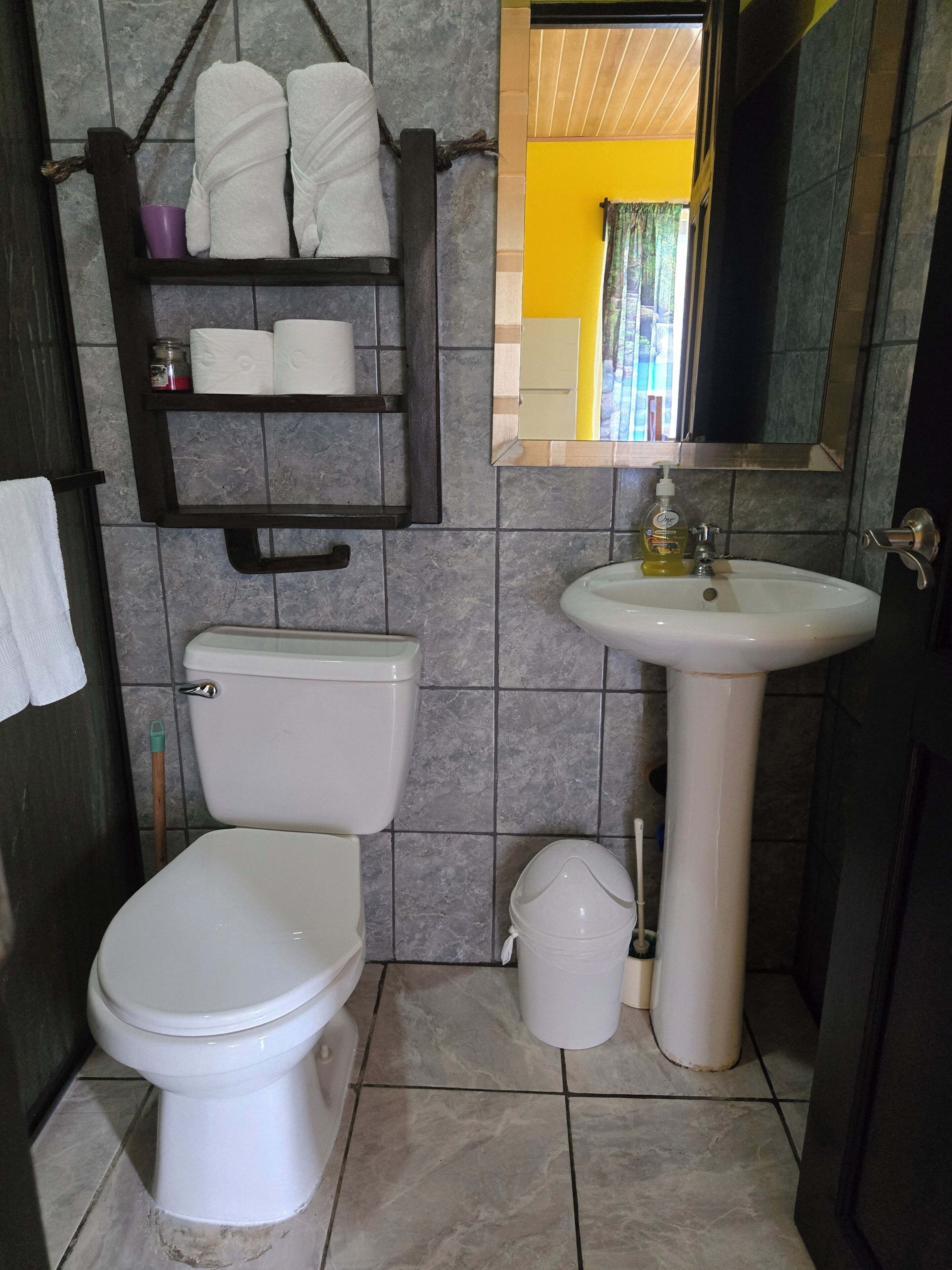 Un bagno con il water, un lavandino e uno scaffale con asciugamani e articoli da toilette.
