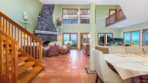 A spacious living area with a stone fireplace, wooden staircase, and a dining table set for four.