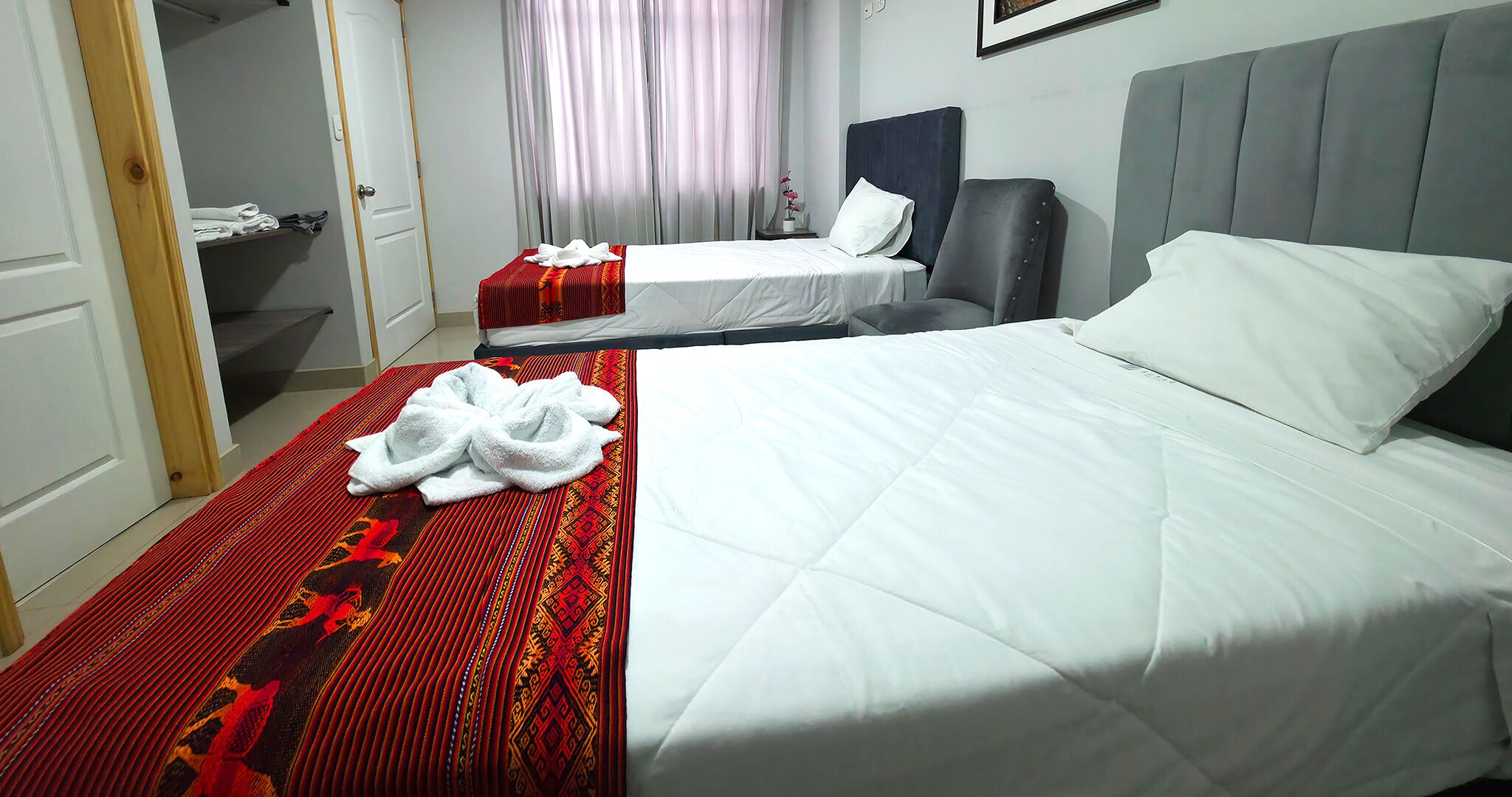 A hotel room with two beds, a red patterned area rug, and a small table with a vase of flowers.